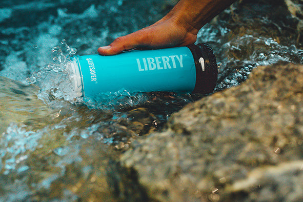 Load image into Gallery viewer, A blue LifeSaver Liberty bottle collecting water from a stream