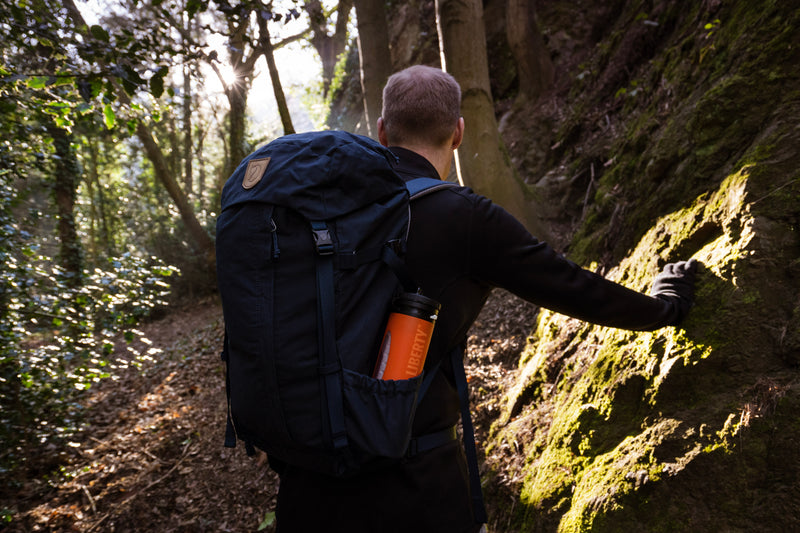 Load image into Gallery viewer, Hiker climbing a steep forest path with an orange LifeSaver Liberty in his backpack
