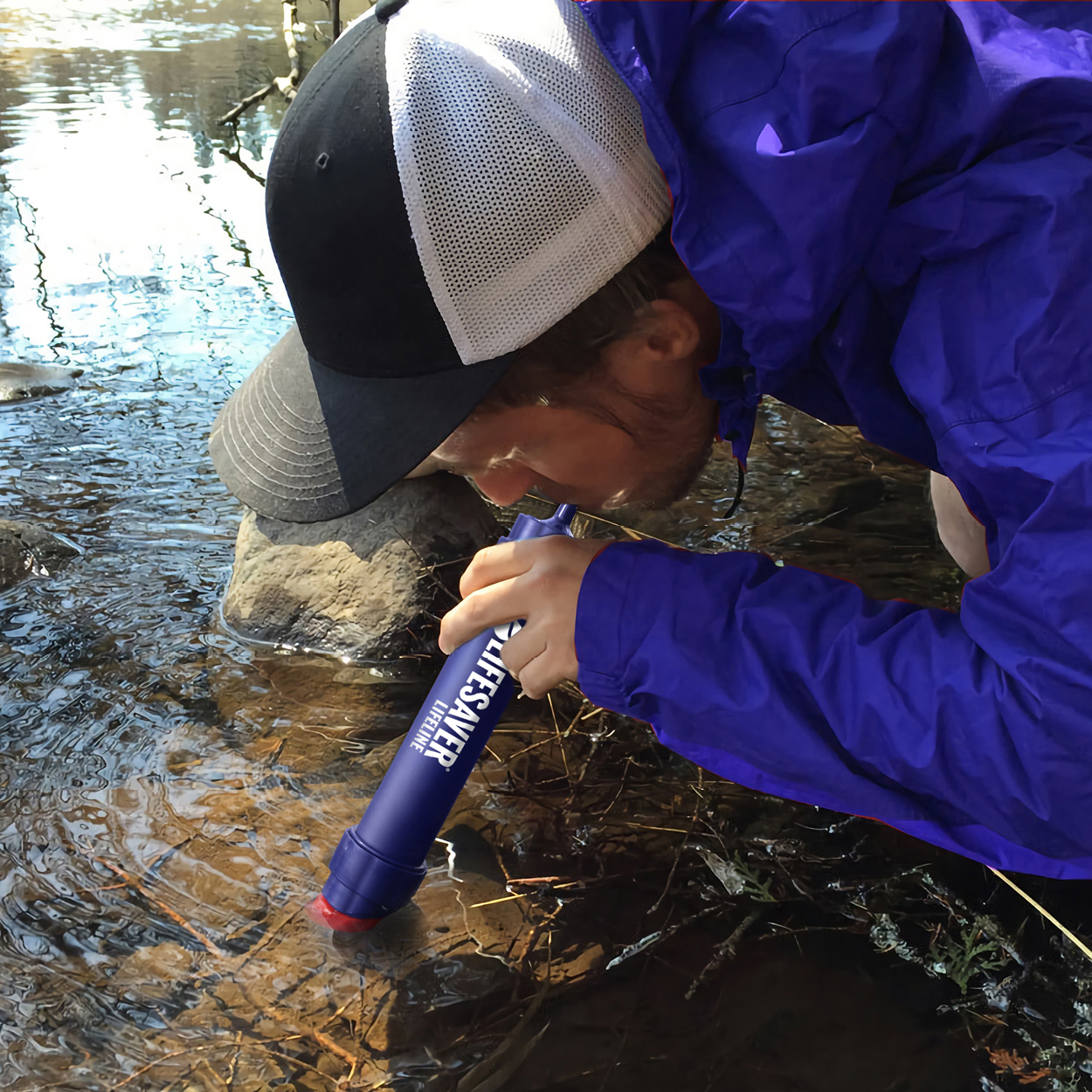 Person in a blue jacket and cap using a water filter device in a stream