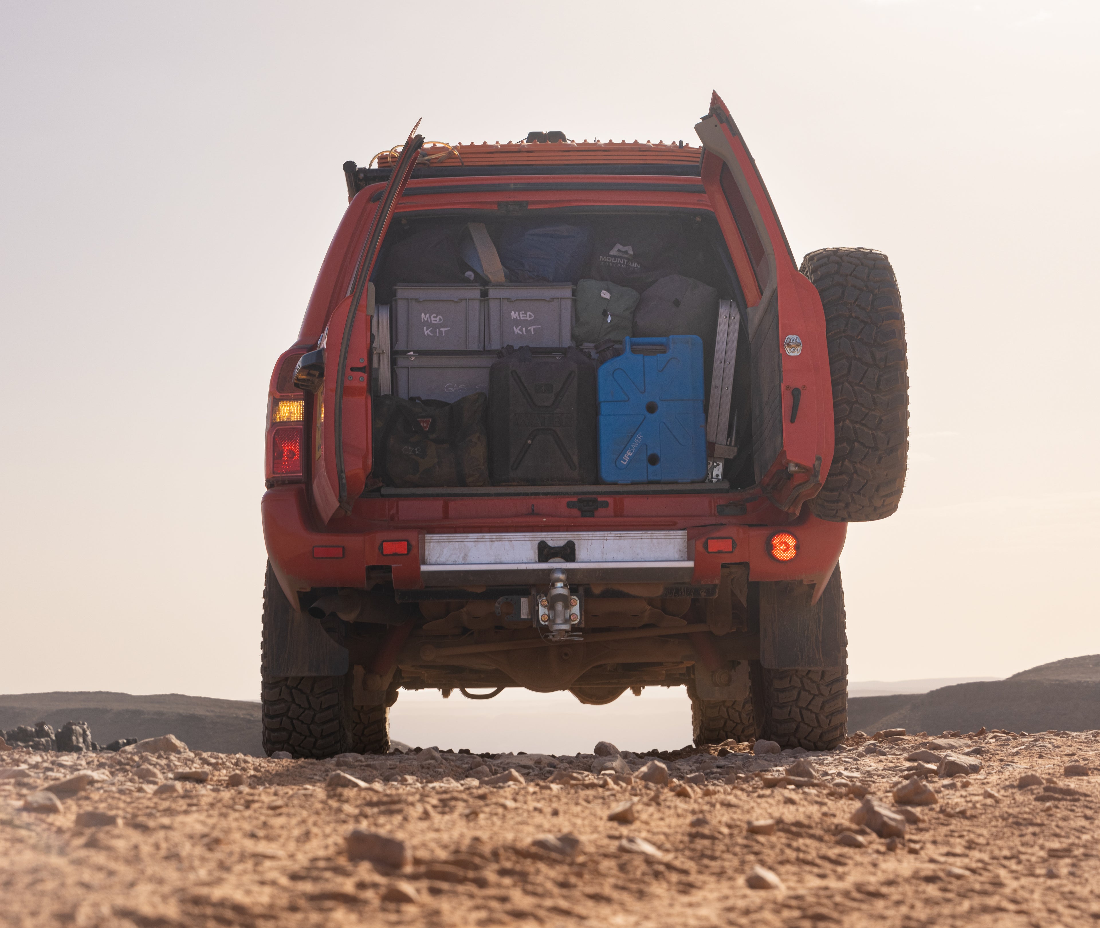 Red off-road vehicle with open doors and a LifeSaver Jerrycan in a desert setting